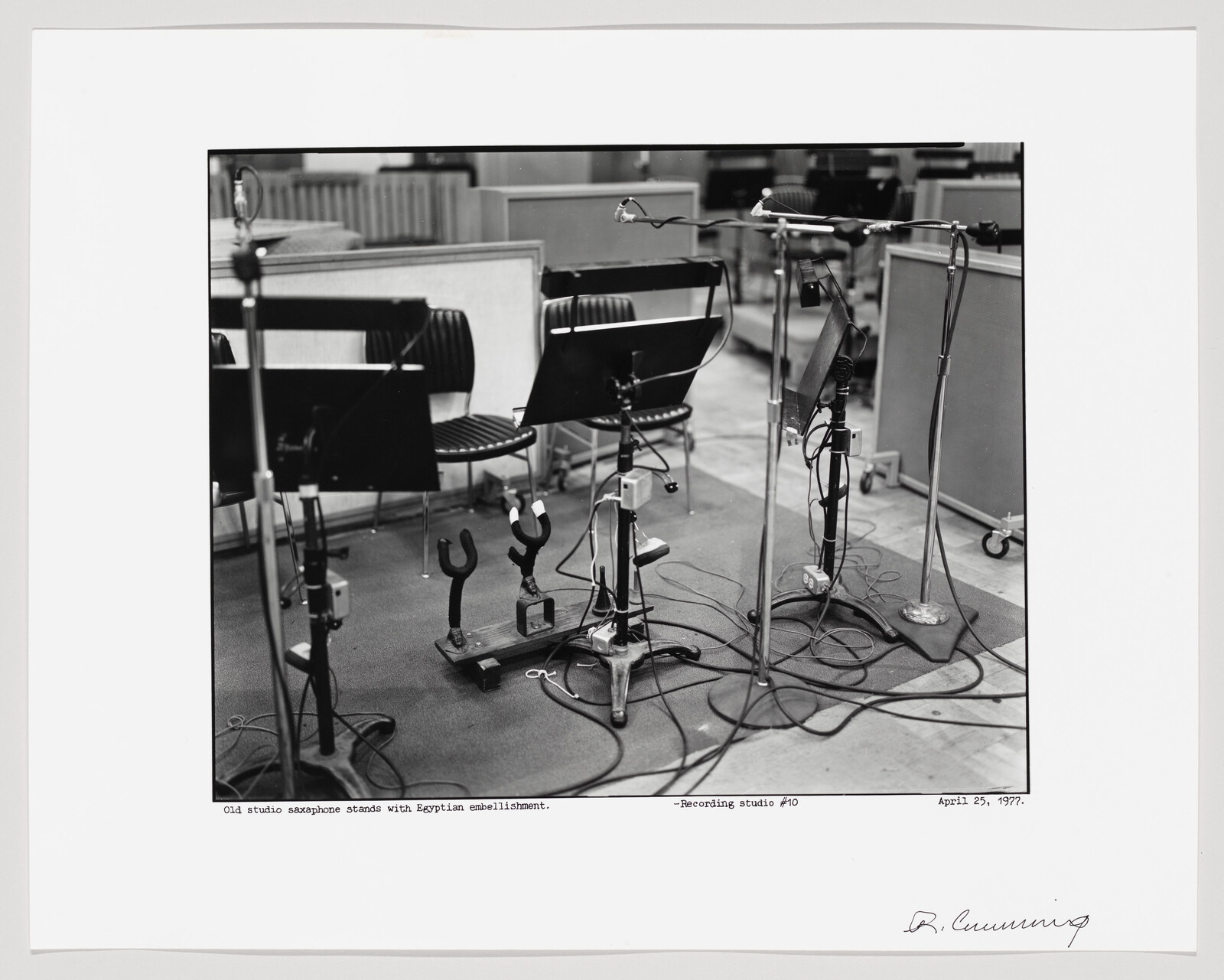Old saxophone stands surrounded by microphones and tangled cables on a recording studio floor.