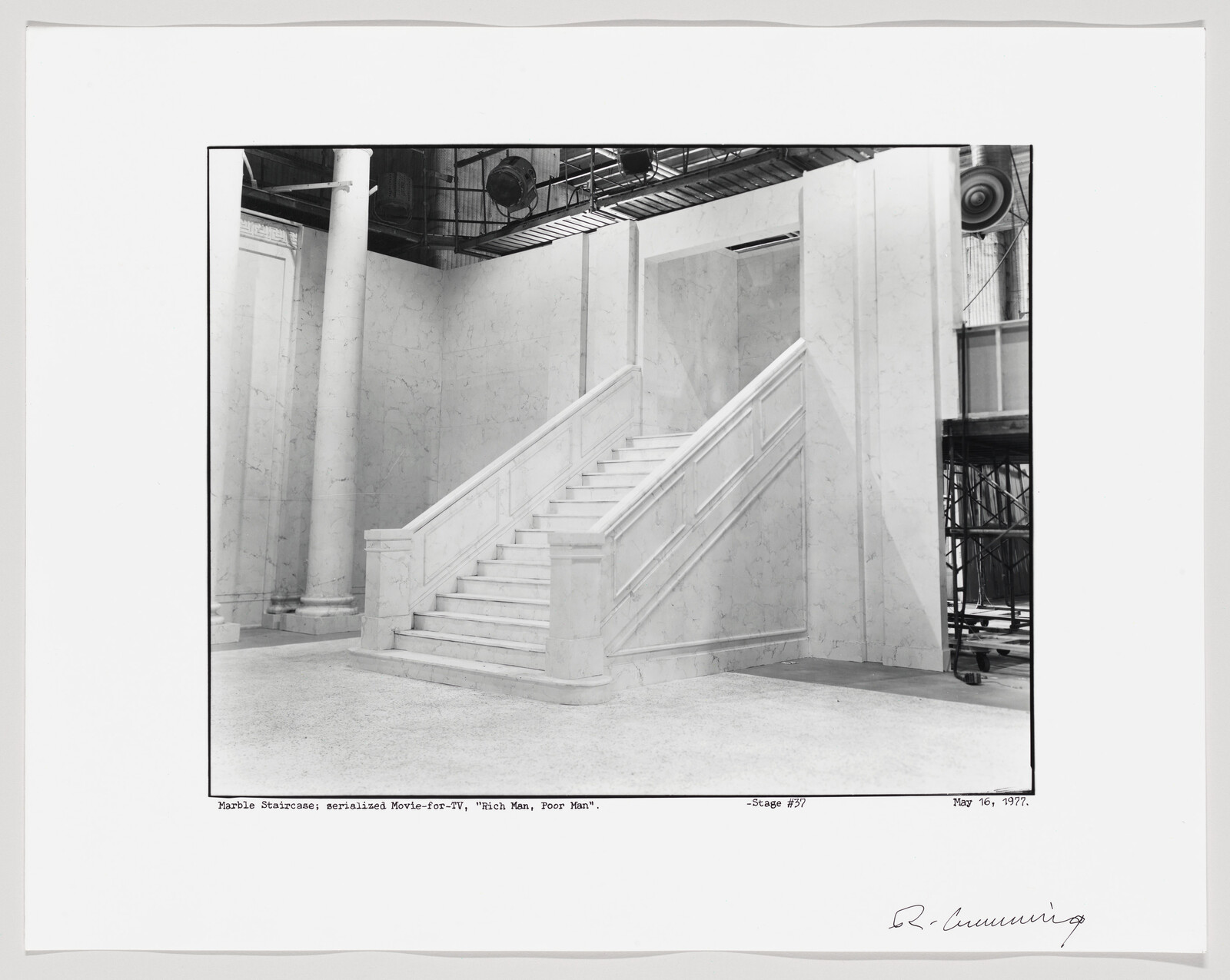A wide marble staircase with paneled railings on a stage set beneath overhead scaffolding.