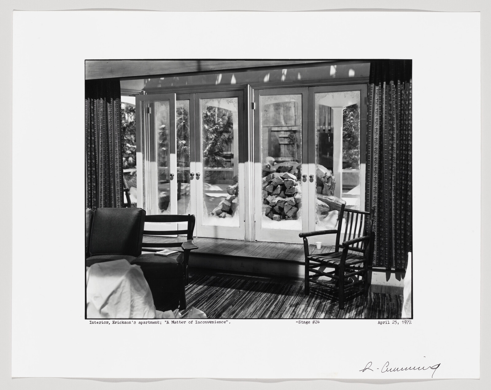Two wooden chairs face glass doors showing a stacked pile of snow-covered firewood outside.