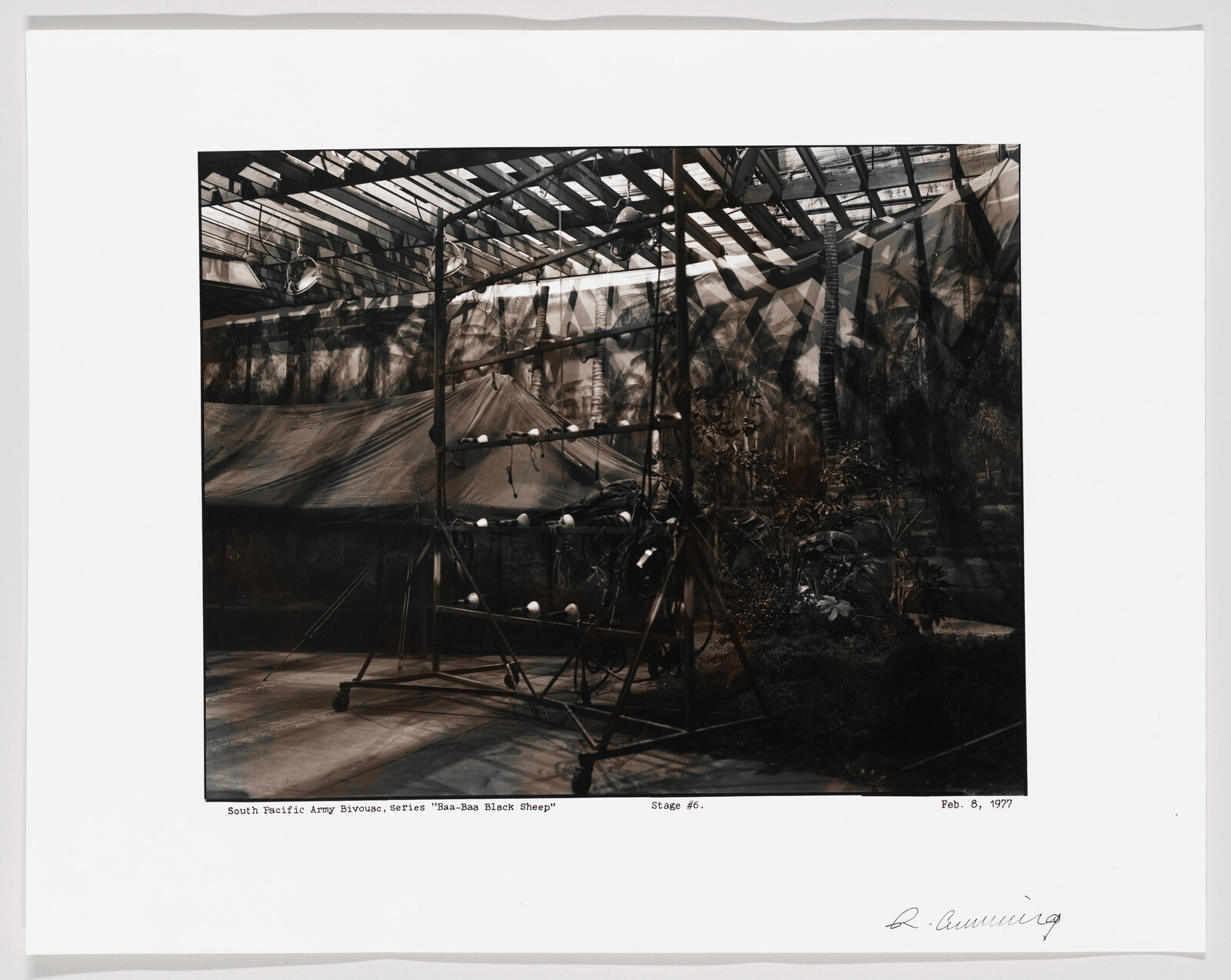 A dim theater set shows a canvas army tent with scaffolding and hanging stage lights.