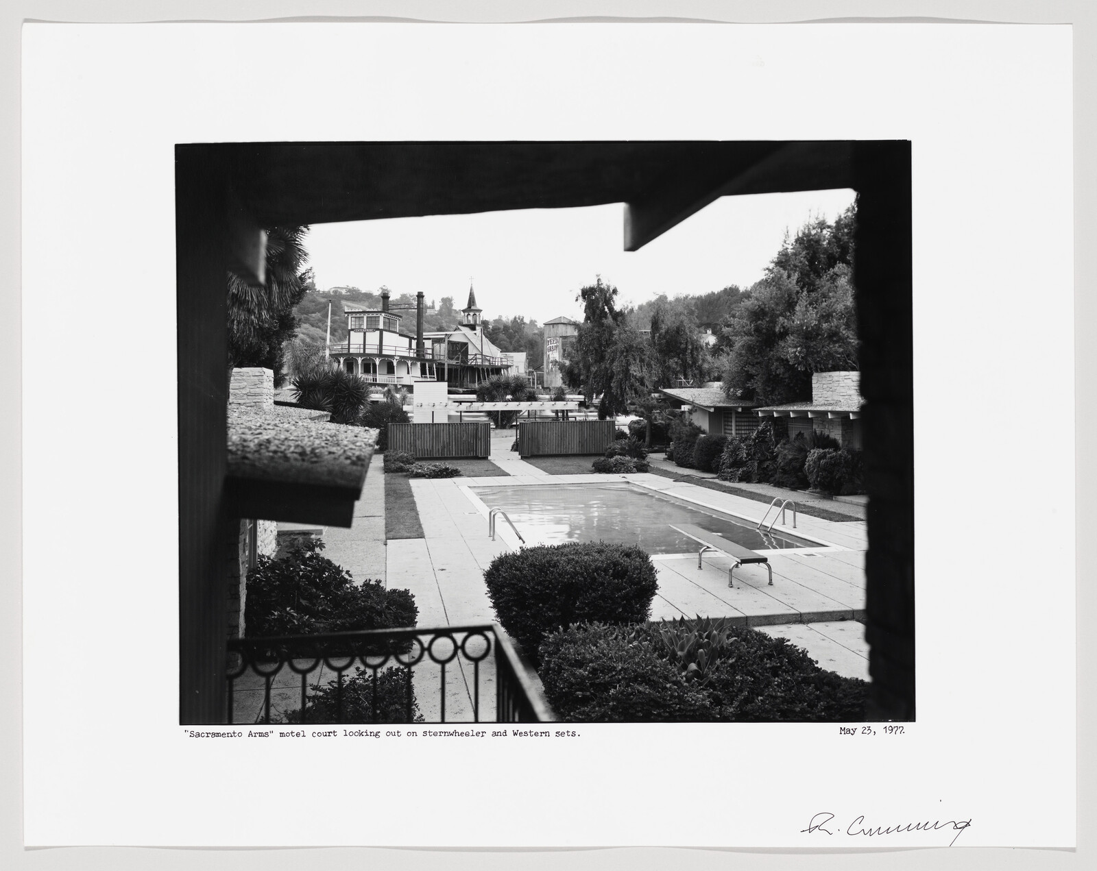 Motel courtyard with empty swimming pool, diving board, and midcentury buildings in the background.