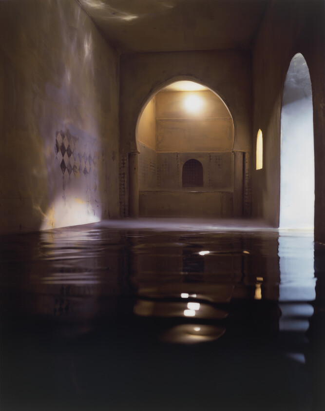 A dim arched room partially filled with still water reflecting soft light from door and niche.