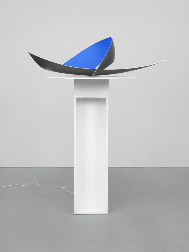 Abstract metal sculpture with blue inner curve rests on a tall white pedestal in a gallery.