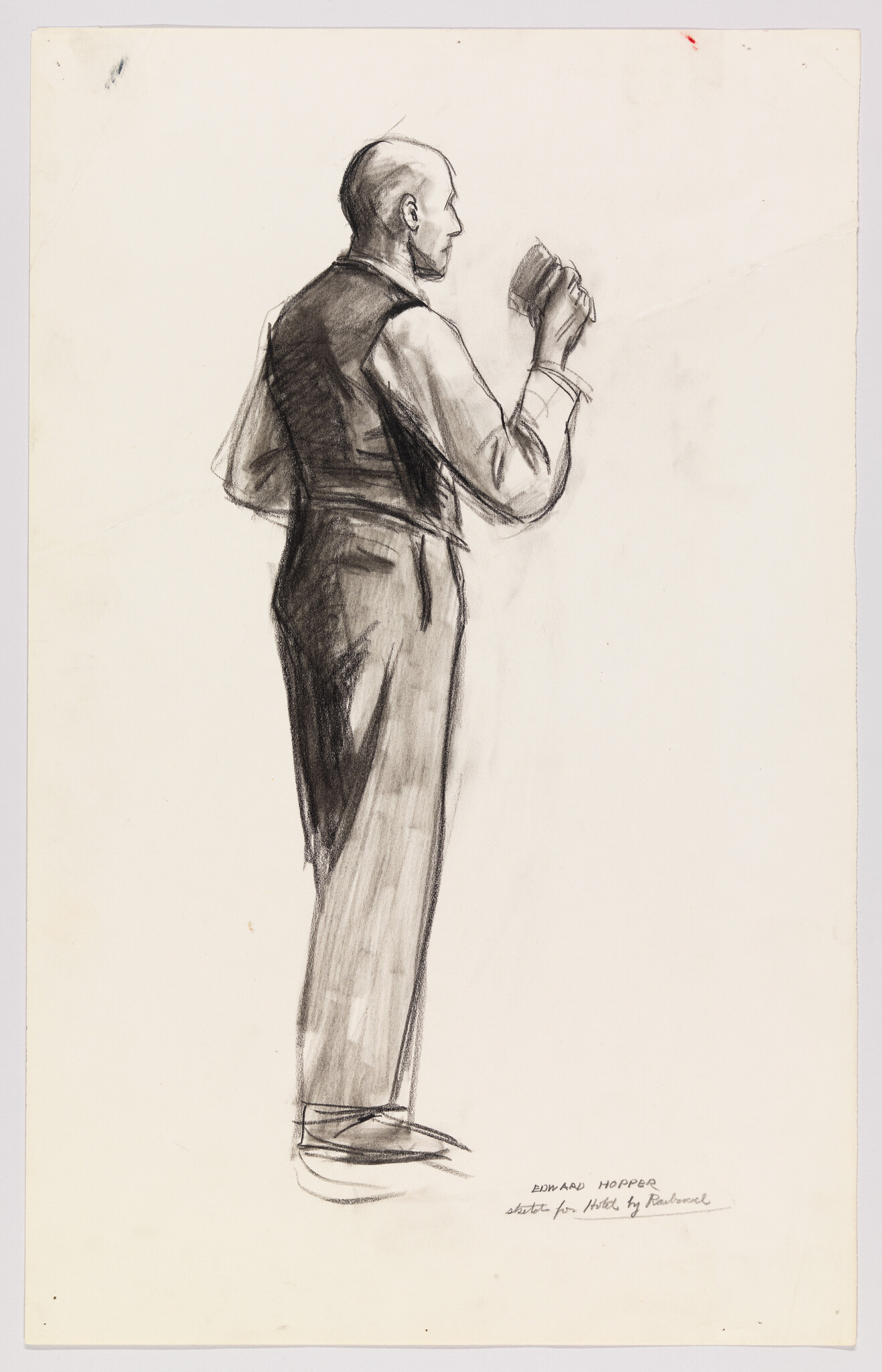 A standing man in a vest holding a hat up in his right hand.