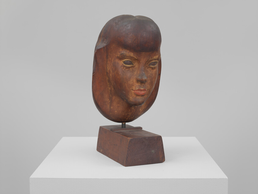 An aged wood sculpture of Alice Compton's head with remnants of paint, atop a wood base.