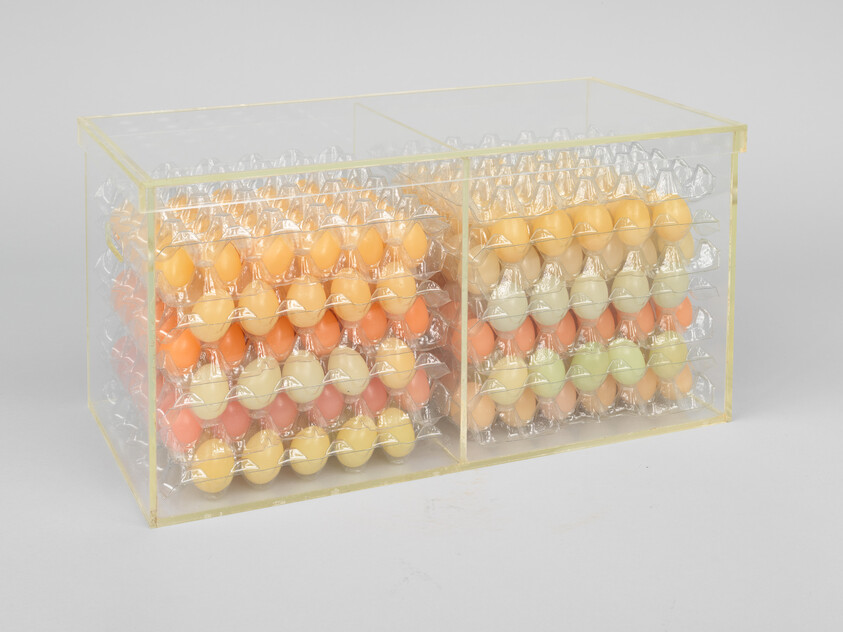 Two clear plastic boxes holding stacked trays of pastel-colored eggs.