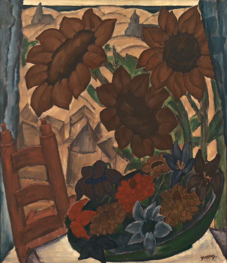 Large dark sunflowers and a bowl of mixed flowers on a table by a window.