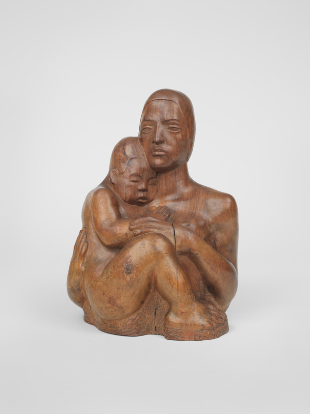 Wooden sculpture of a mother tenderly holding a sleeping child in her arms.