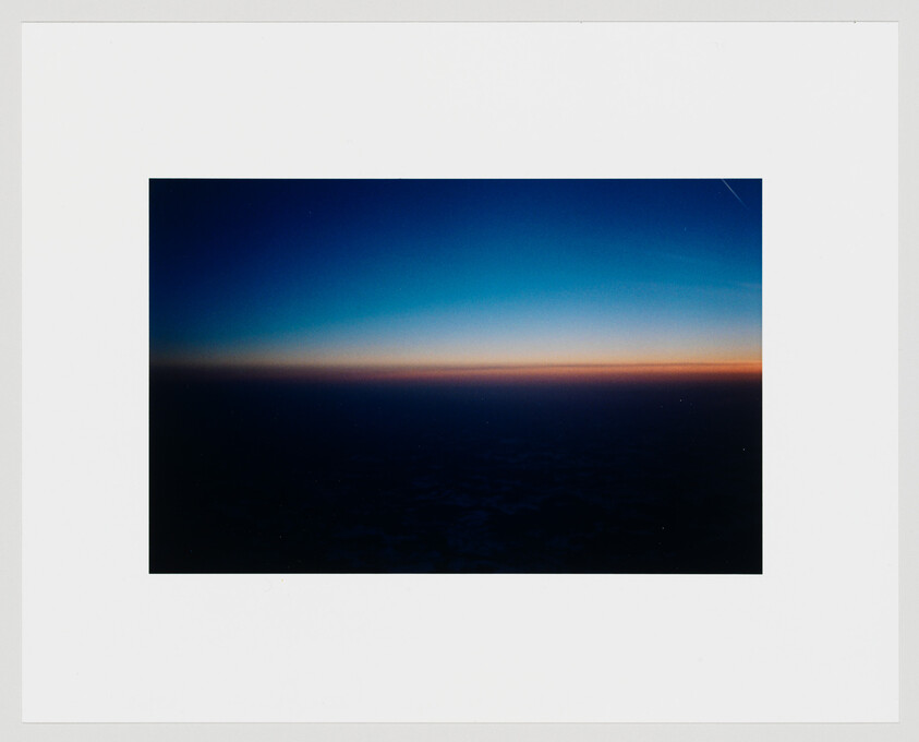 A dark horizon with a thin orange glow under a deep blue sky during sunrise.