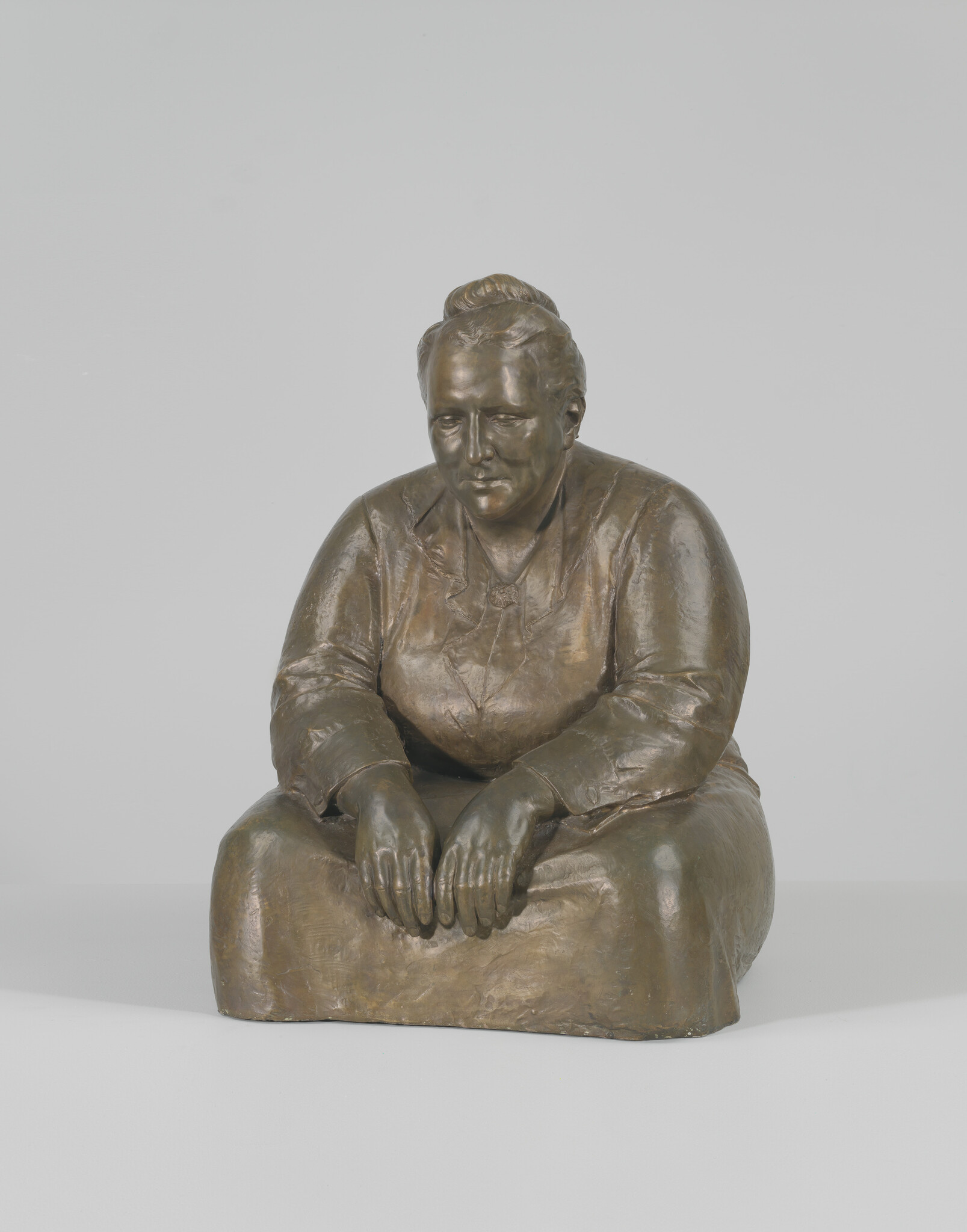 A bronze sculpture of a seated woman resting her hands and looking downward.