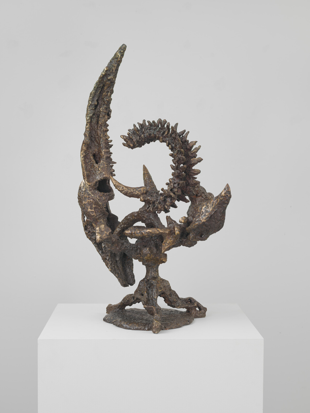Bronze abstract sculpture with twisted, spiky loop and horn-like forms standing on a white plinth.