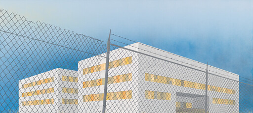 A guarded white building with lit windows stands behind a high chain-link fence topped with barbed wire.