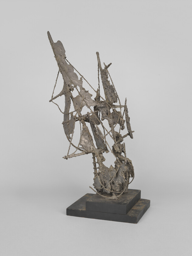 Abstract tangled metal sculpture with sharp angles and open framework mounted on a stepped black base.