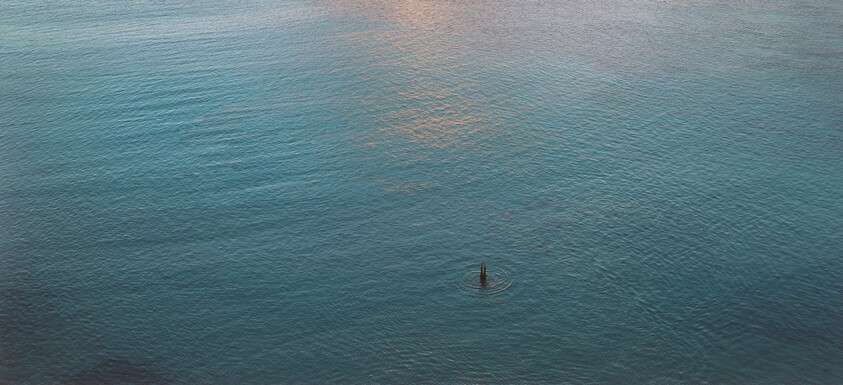 A solitary buoy floating in calm blue water with small ripples around it.