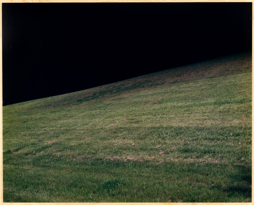 A gently sloping grassy hill rising into a dark, empty sky.