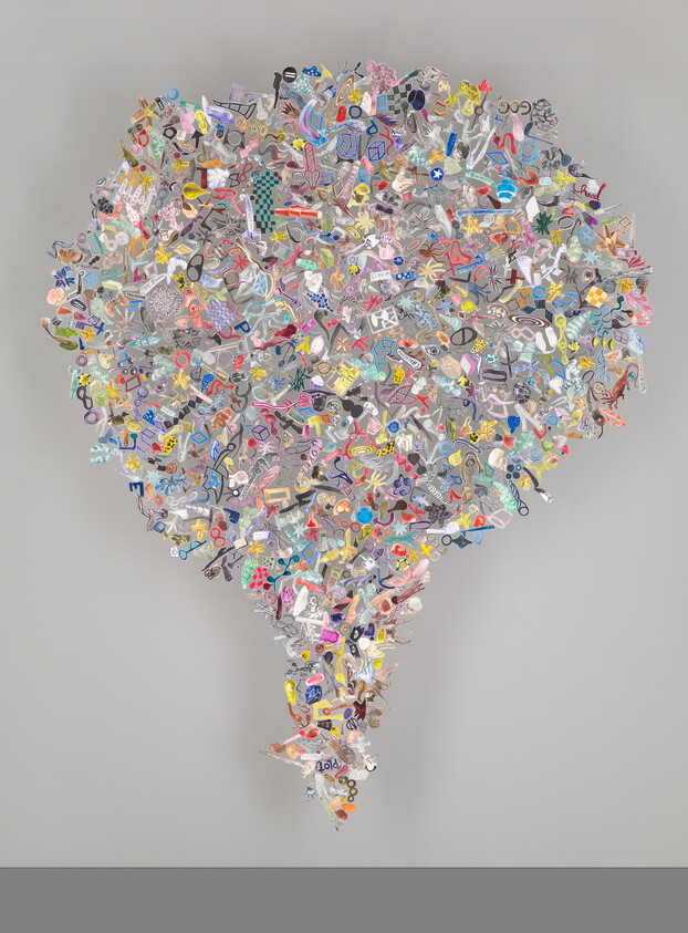 Large colorful cluster of small objects forms an inverted teardrop sculpture against a gray wall.