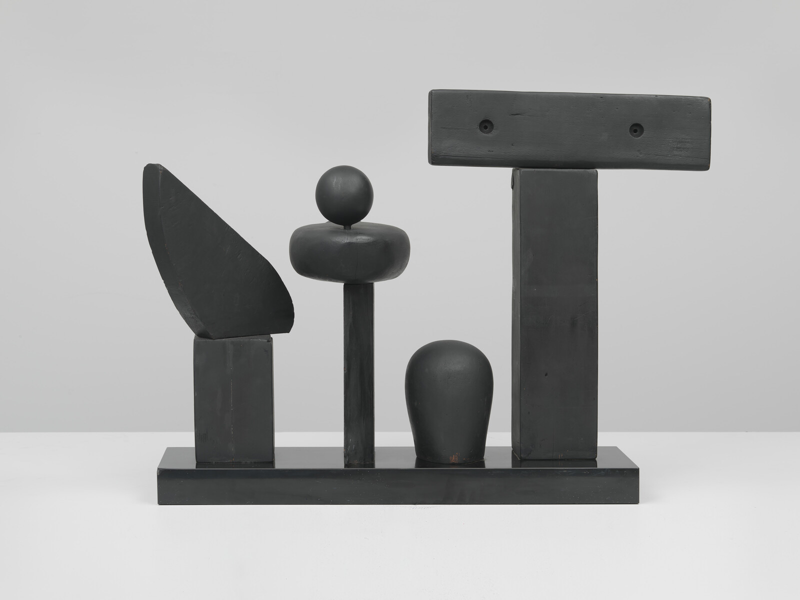 Black wooden abstract sculpture with geometric blocks, a sphere on a column, and a T-shaped beam.