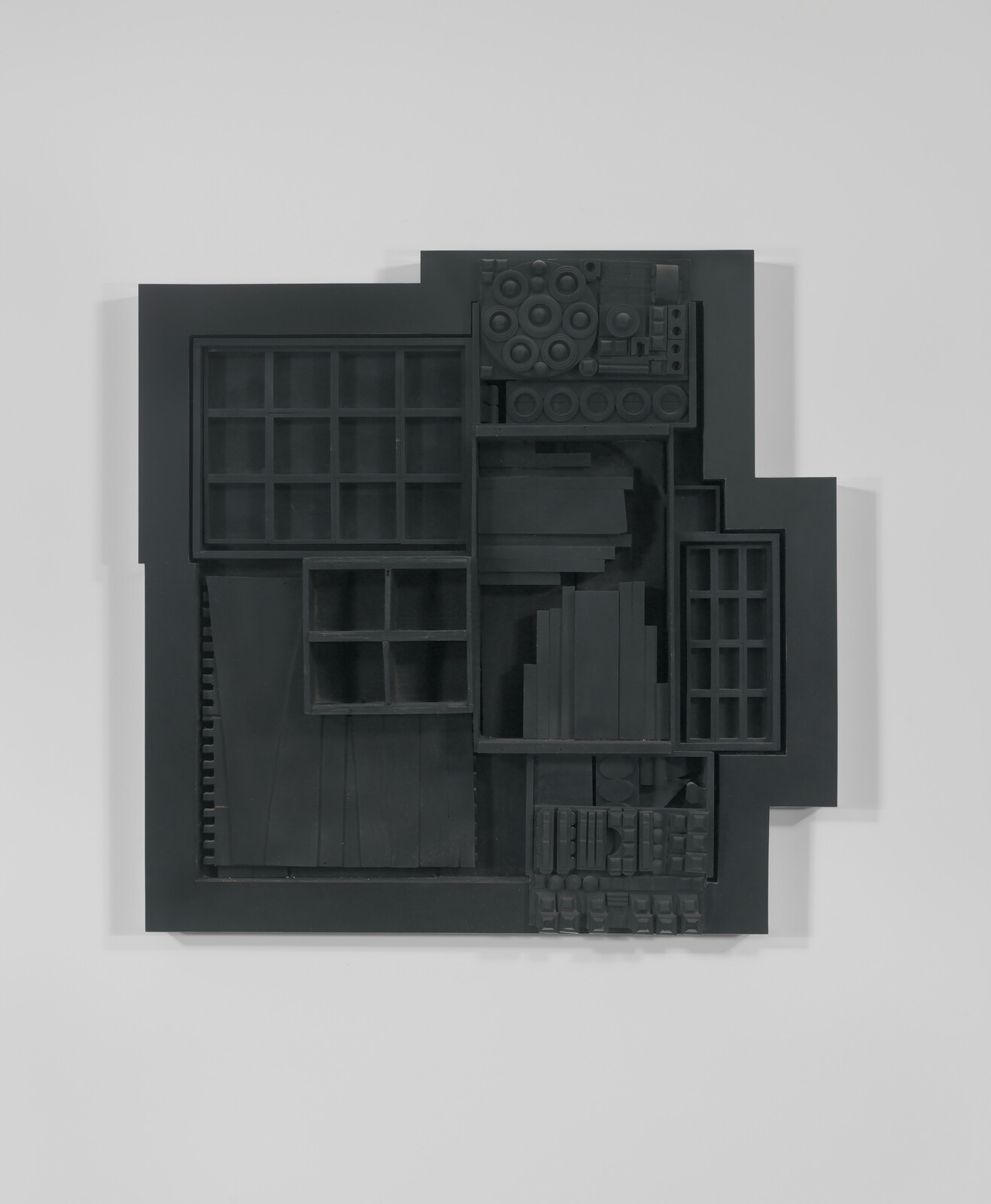 Black geometric wall sculpture composed of nested rectangular compartments and varied circular and block shapes.