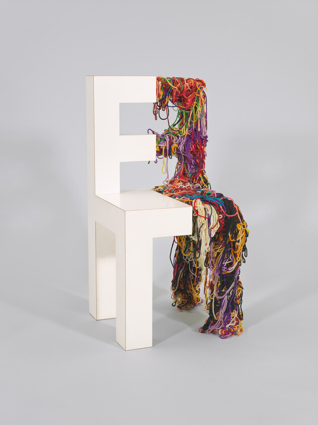 White modern chair partially covered and dripping with colorful tangled yarn strands.