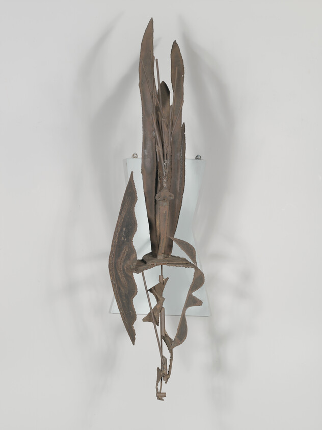 Abstract rusted metal sculpture resembling tall plant mounted on a frosted glass wall panel.