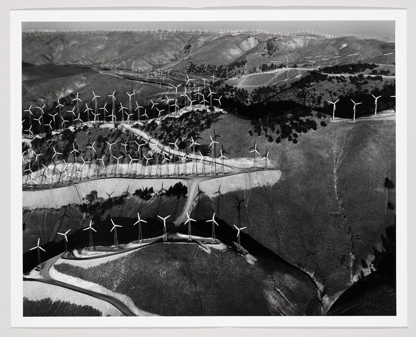 Rows of wind turbines stretch across rolling hills in an aerial view of a wind farm.