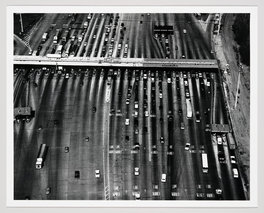 Aerial view of a wide toll plaza with many cars approaching manned lanes.