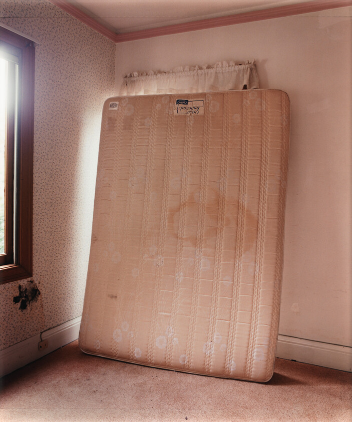 A stained old mattress leaning upright against a faded wall in an empty bedroom.