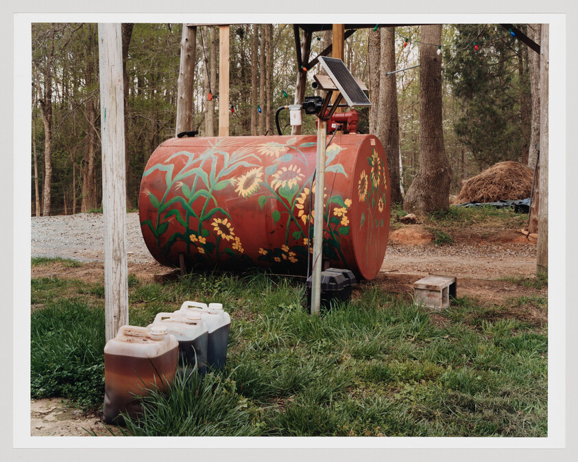 Large red fuel tank painted with sunflowers sits near a solar-powered pump and jerry cans.