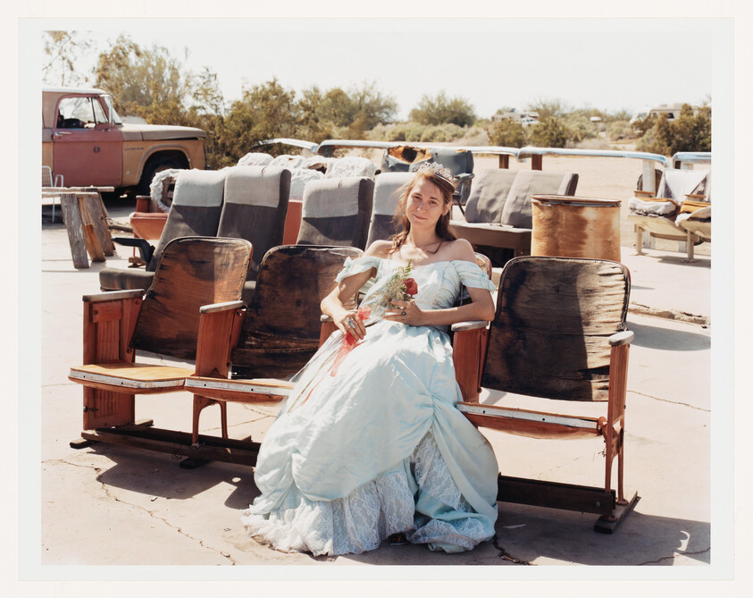 Young woman in a light blue prom dress sits on old theater seats outdoors holding a bouquet.