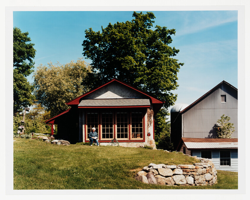 Small red-trimmed cottage with large windows and a person sitting on the front steps.