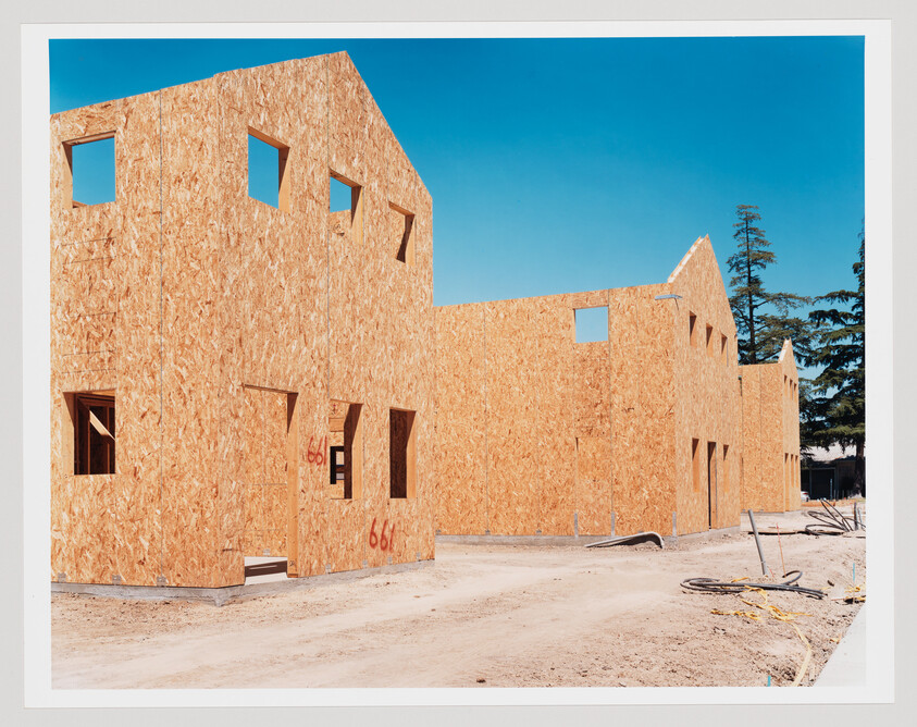 Row of wood-framed house shells under construction against a clear blue sky.