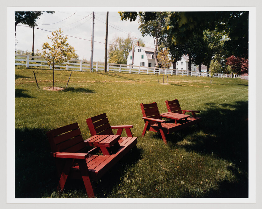 Three red wooden lawn chairs arranged on grass near a white fence and house.