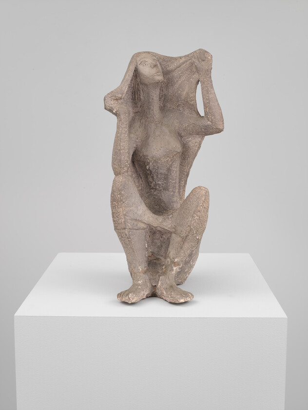 A crouching clay sculpture of a woman lifting cloth or hair above her head on a pedestal.