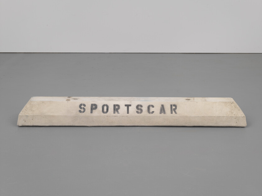 A concrete parking curb with the word "SPORTSCAR" stenciled across its front.