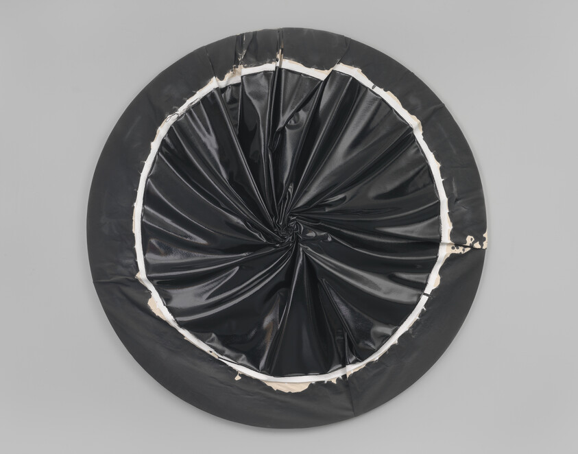 Round black vinyl disc gathered into a central twist with torn white inner edge on gray wall.