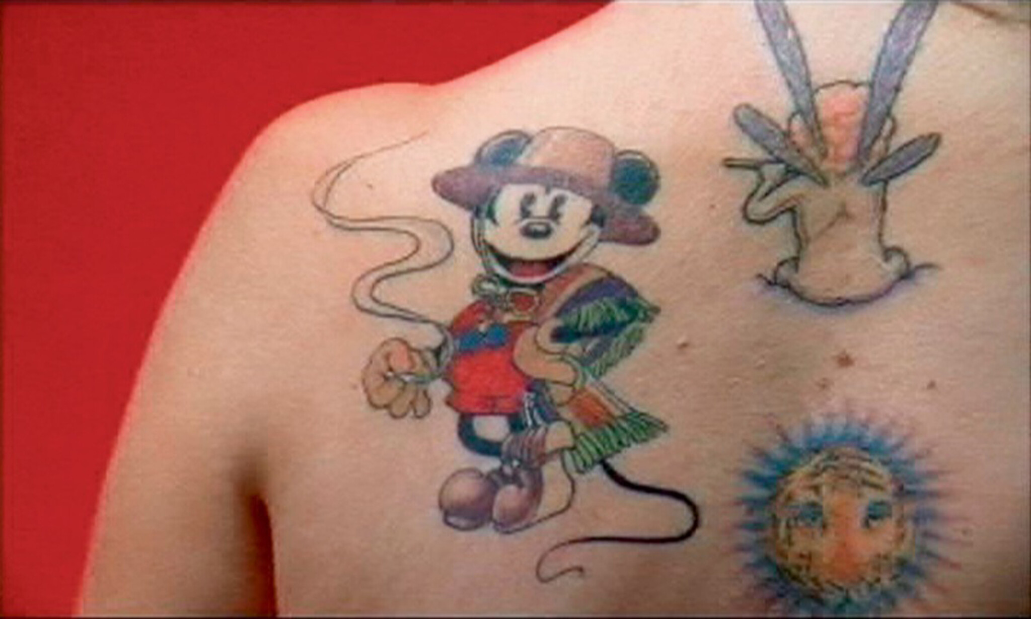 A chest tattoo of Mickey Mouse wearing a hat and poncho while holding a smoking cigarette.