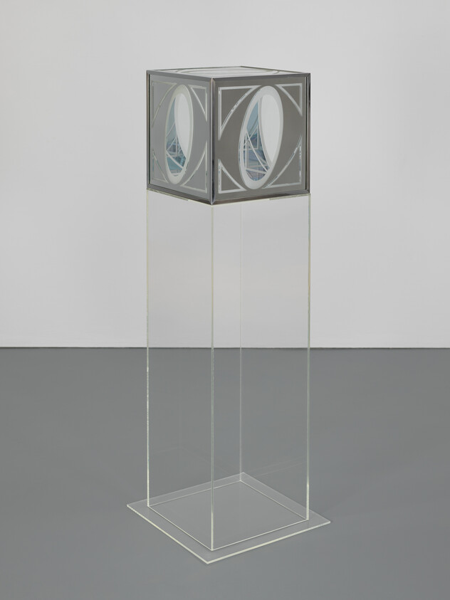 A transparent cube sculpture with intricate geometric patterns and a smaller cube suspended inside, all mounted on a clear pedestal against a white background.