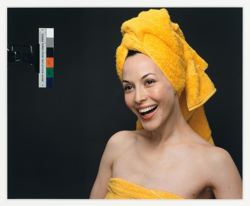 A smiling woman wears a bright yellow towel wrapped on her head and around her body.