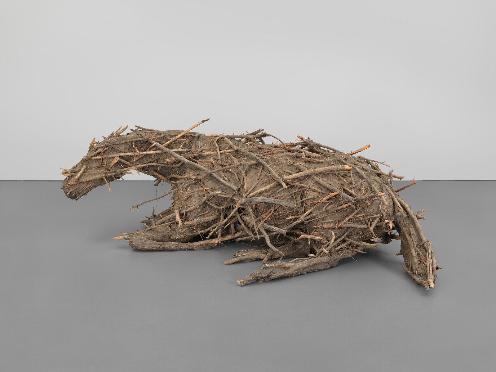 Large animal sculpture made from sticks and branches, shaped to look like a crouching or resting creature.