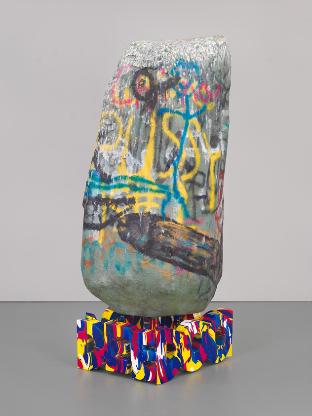 Tall graffiti-covered stone sculpture balanced on a multicolored painted block base.