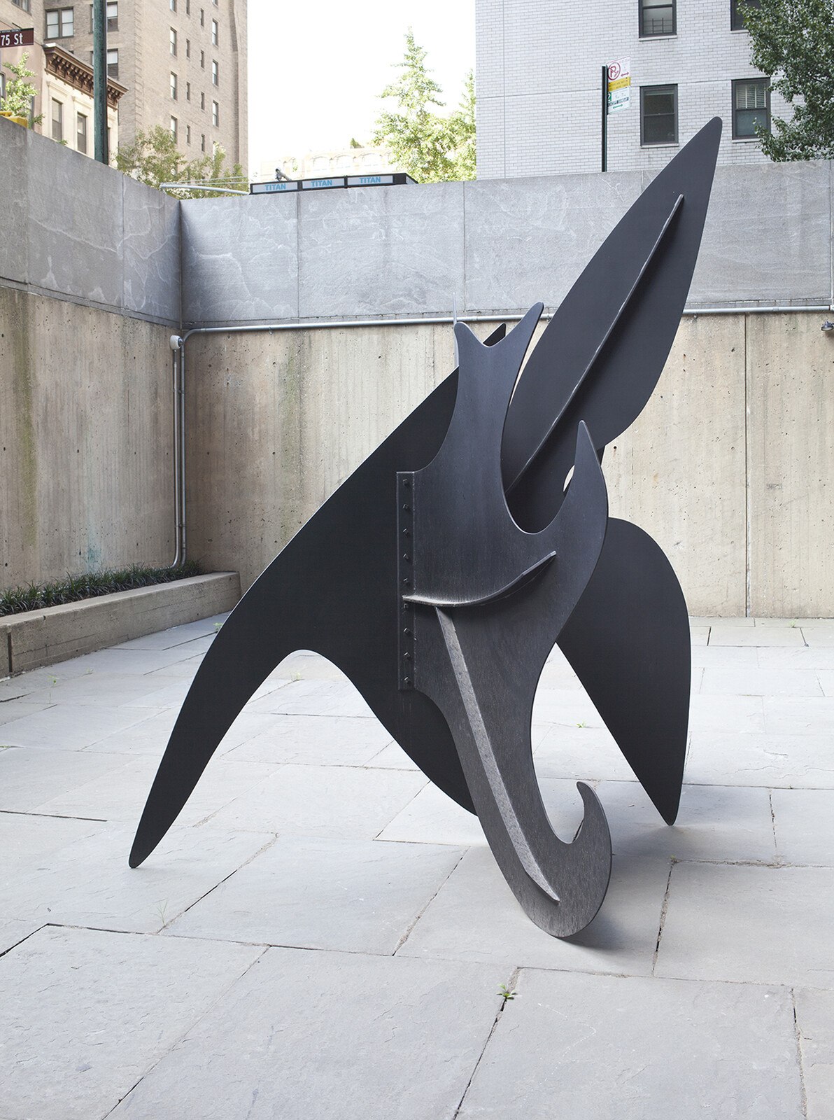 Large abstract black metal sculpture with curved and pointed shapes standing on a stone courtyard.