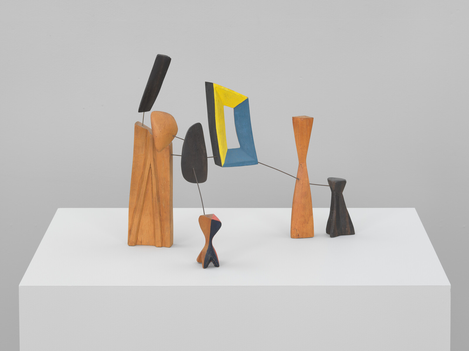 Abstract wooden mobile with colorful geometric pieces balanced on thin metal rods atop a pedestal.