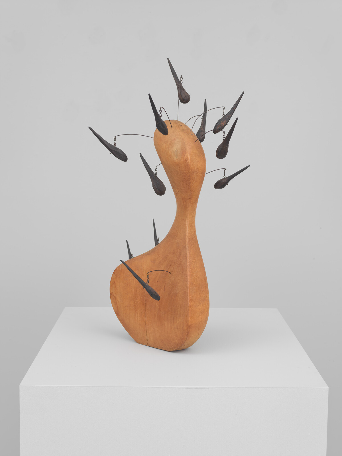 A smooth wooden abstract sculpture with multiple dark metal teardrops on thin wires extending outward.