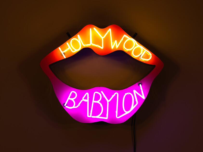 A neon sign of lips with the word "Hollywood" written across the top lip in orange and "Babylon" aganist the bottom lip in purple