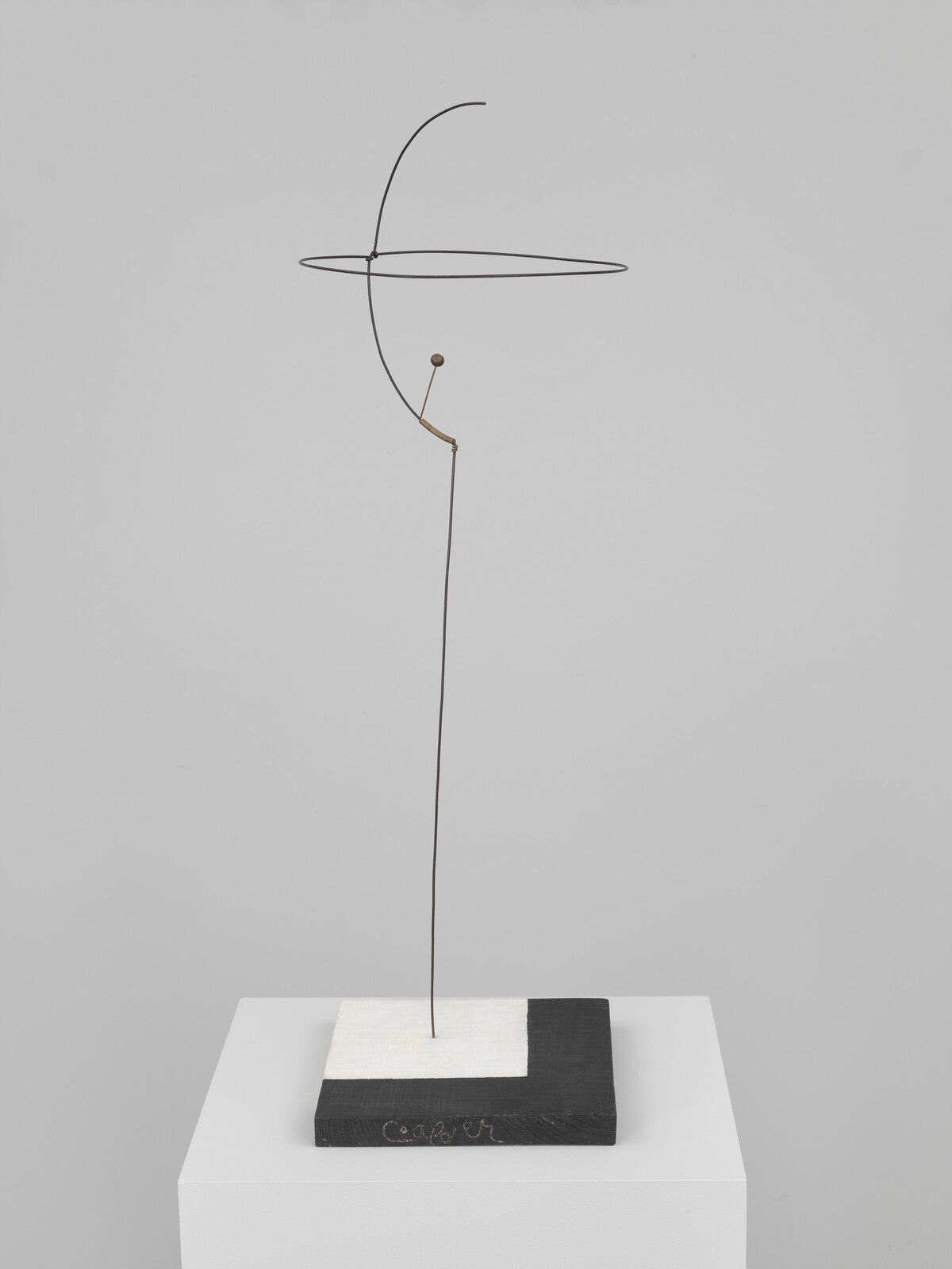 Thin wire mobile sculpture balances a circular loop above a tall vertical rod on a square base.