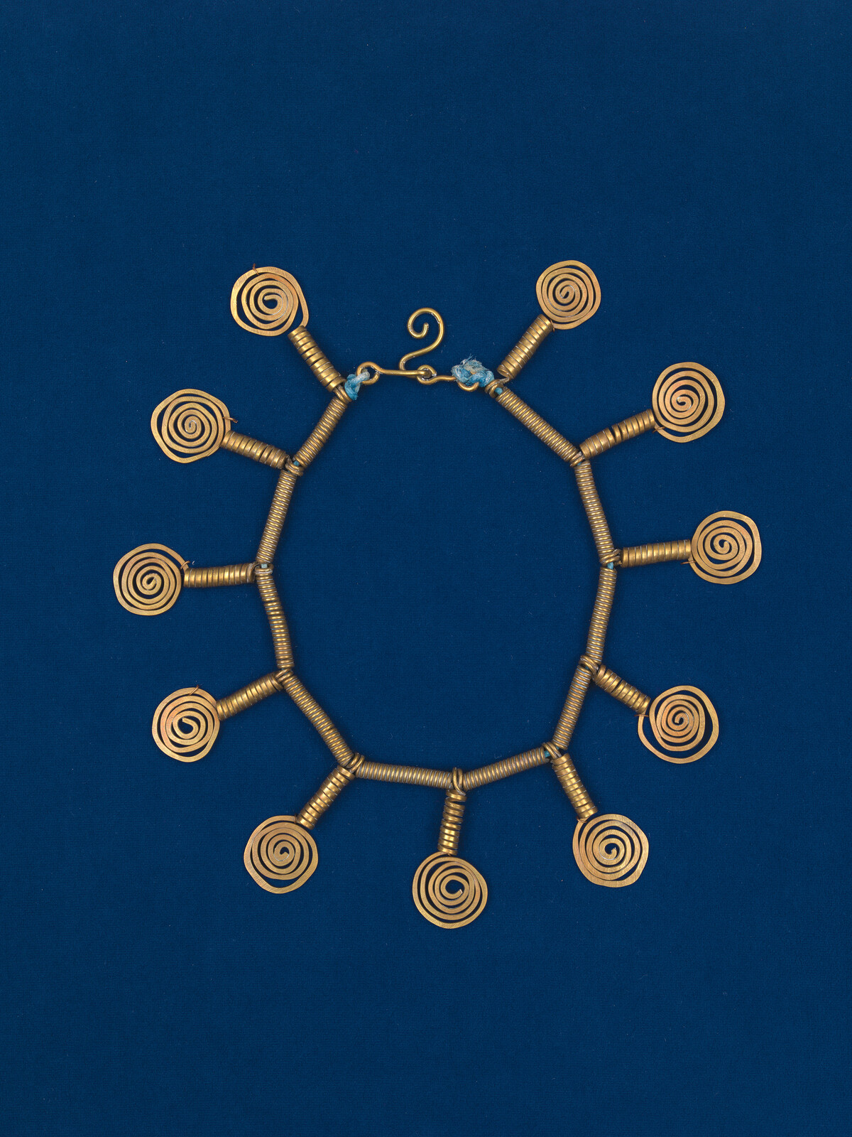 Gold coil necklace with repeated spiral charms arranged in a circular pattern on a blue background.