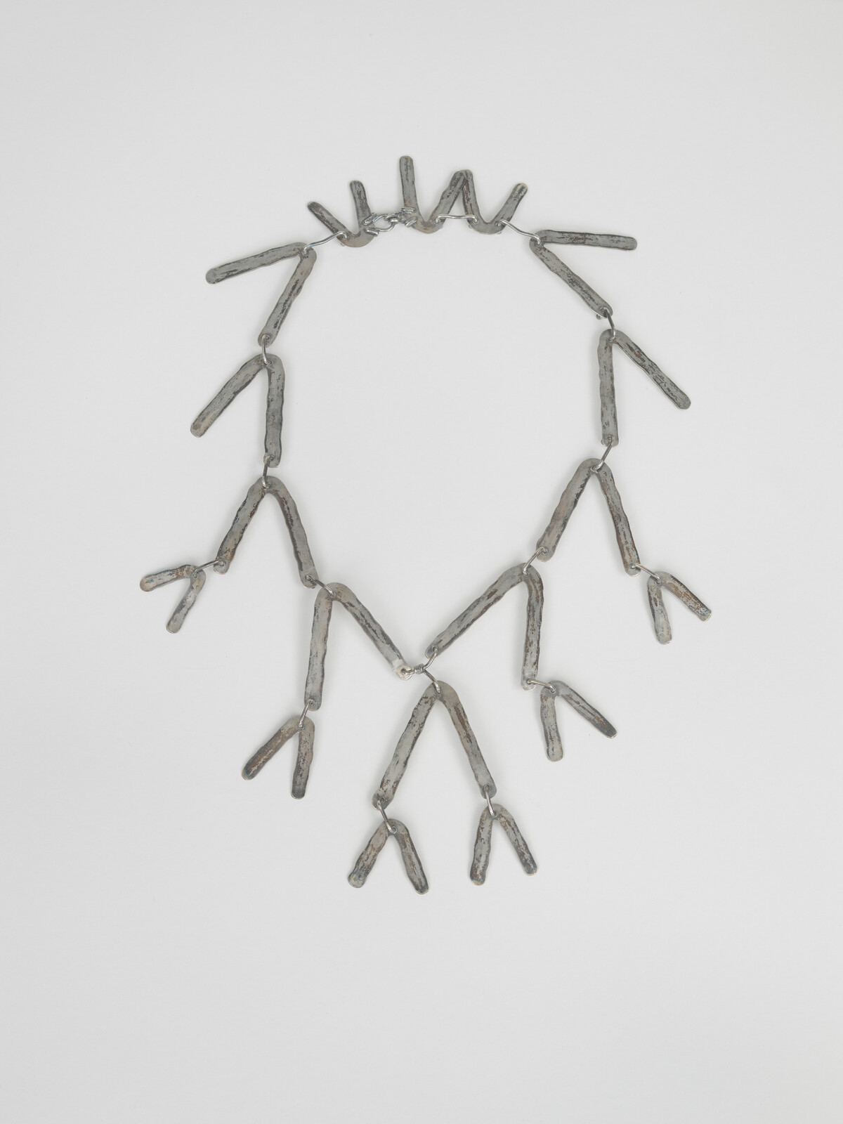 A silver-tone necklace made of linked twig-like pieces forming multiple V-shaped hanging branches.