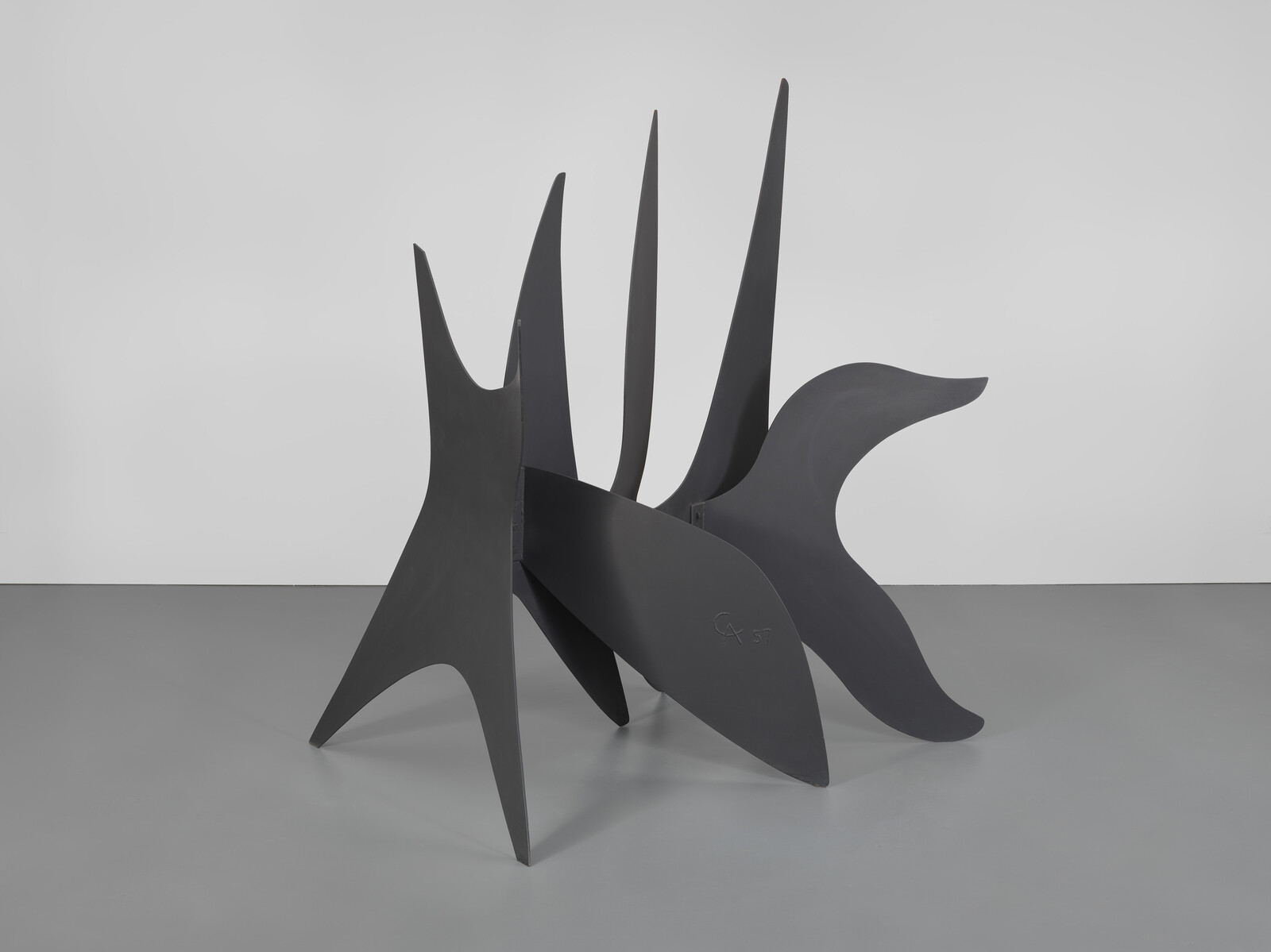 Black abstract metal sculpture with tall pointed and curved panels standing on a gallery floor.