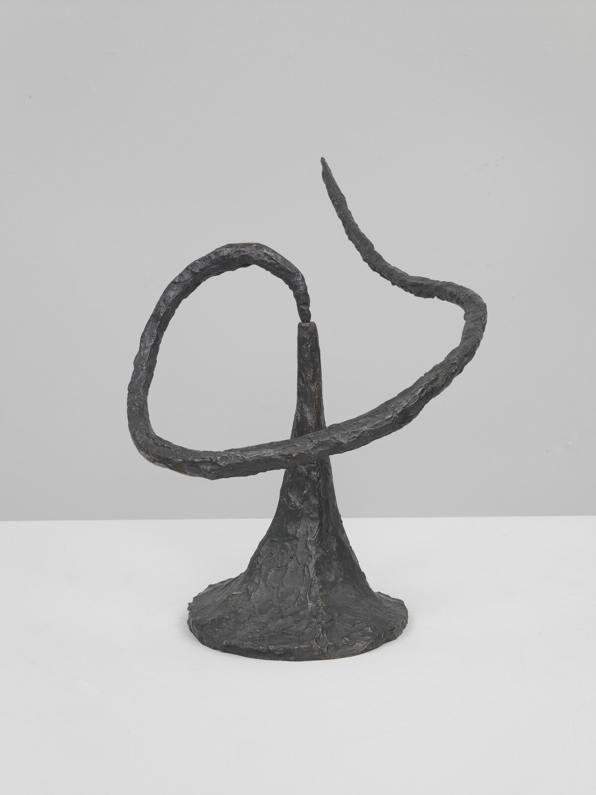 A dark, textured metal sculpture with a conical base and a looping curved arm extending upward.