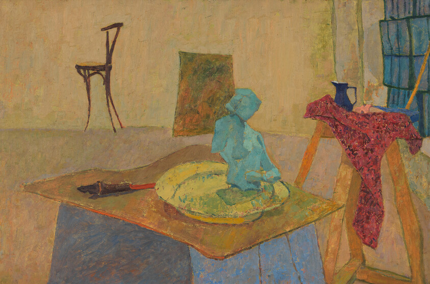 A blue clay figure sits on a plate on a studio table with a red cloth draped nearby.